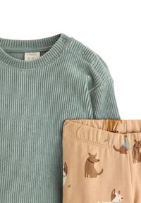 Lyseblå ribbet langærmet top med trykknapper, parret med beige bukser med hundemønster i brun og creme. Blødt bomuldsstof.