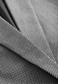 Tissu gris avec un motif pied-de-poule, présentant un tissage serré et une texture lisse. L'image capture des couches de matériel superposées.