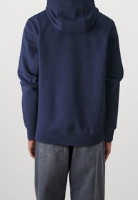 Sudadera con capucha azul marino de corte relajado, con puños y dobladillo acanalados; combinada con pantalones de mezclilla gris claro que tienen bolsillos traseros.