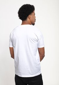 Hvid bomulds t-shirt med korte ærmer, en rund halsudskæring og en glat tekstur, vist fra ryggen mod en ensfarvet baggrund.