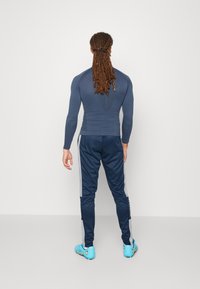Navy langermet treningstopp paret med matchende bukser, med en elegant design og blå joggesko med gule accenter.