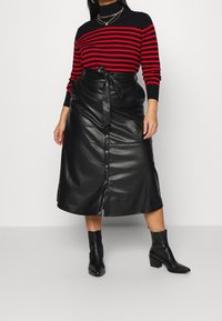 Gonna midi in ecopelle nera con vita legata, caratterizzata da una chiusura a bottoni e una texture liscia, abbinata a un maglione a righe rosse e nere.