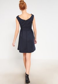 Mörkblå ärmlös klänning med ett figursytt liv, utsvängd kjol och dragkedja i ryggen. Slät tyg med rena linjer och minimalistisk detaljering.