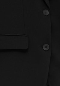 Svart blazer med en slät tygtextur, en spetsig krage och en enda bröstficka med två svarta knapplås.