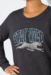 Schwarzes Langarm-T-Shirt mit einem grafischen Druck eines laufenden Leoparden mit metallischen Details und dem Text "BLEIB Wilde UND FREI."