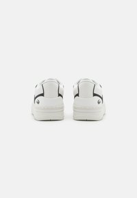 White sneakers with black accents, smooth synthetic material, rounded toe, low-top design, and flat rubber sole, featuring a logo at the heel.