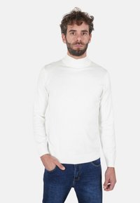 Maglione dolcevita bianco realizzato in materiale a maglia liscia, design aderente, maniche lunghe e polsini a coste, abbinato a jeans scuri.