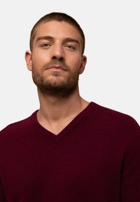 Burgundowy sweter w serek, wykonany z miękkiej wełny, z wykończeniem w prążki przy dekolcie i dopasowanym kroju, prezentowany na jednolitym białym tle.