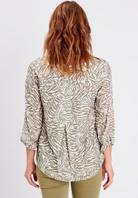 Blouse légère à motifs présentant un design à rayures zèbres vertes et blanches, avec des manches retroussées 3/4 et une coupe décontractée. Idéale pour un look décontracté.