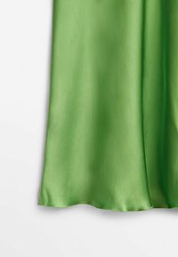 Tissu en satin lisse vert clair drapé verticalement avec des plis doux, présenté sur un fond blanc uni.
