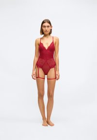 Rød blonde bodysuit med V-hals, justerbare stropper, gjennomsiktige paneler og strømpeholderstropper, med blomsterdesign og intrikate detaljer.