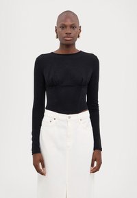 Zwart cropped top met lange mouwen en een gestructureerde afwerking, gecombineerd met een hoge taille witte dennen rok met een voorkap en metalen accenten.
