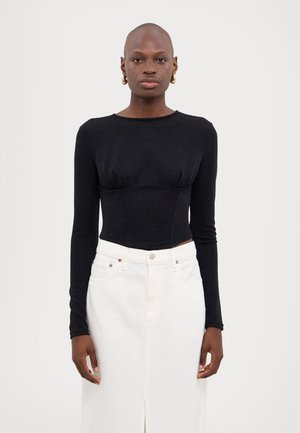 Haut noir à manches longues et coupé avec une finition texturée, associé à une jupe en denim blanche taille haute avec une fente à l'avant et des accents métalliques.