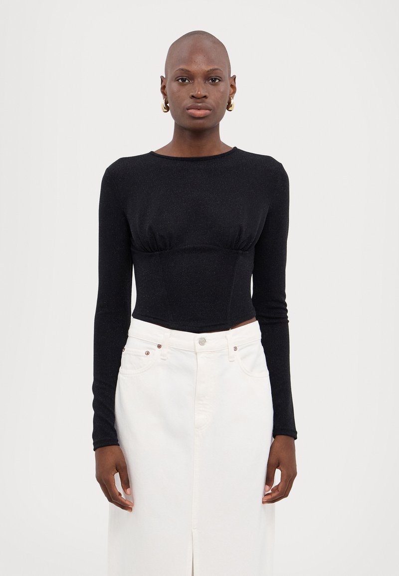 Zwart cropped top met lange mouwen en een gestructureerde afwerking, gecombineerd met een hoge taille witte dennen rok met een voorkap en metalen accenten.
