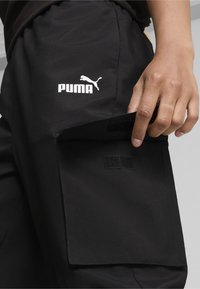 Zwarte broek met een zijzak met klittenbandsluiting. Het Puma-logo is duidelijk zichtbaar in het wit op het bovenbeen.