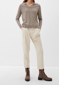 Pull à col en V marron clair associé à un pantalon côtelé crème et des bottines à lacets marron. La tenue présente une coupe décontractée et des textures douces.