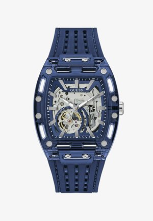 Ceas de mână Blue Guess cu față transparentă care arată mecanismul automat, ace și marcaje argintii, cu curea albastră din silicon perforat.