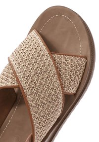 Woven straw slide sandal with brown leather accents, featuring cross-band design and textured surface, mounted on a cushioned sole.