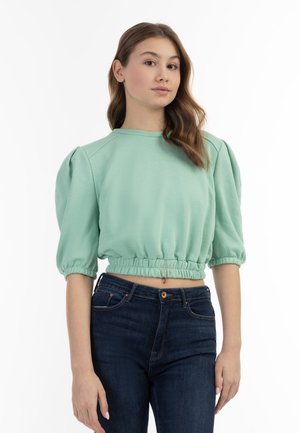 Myntegrøn cropped sweatshirt med puffede korte ærmer og en rynket talje, parret med mørkeblå jeans. Glat stoftekstur.