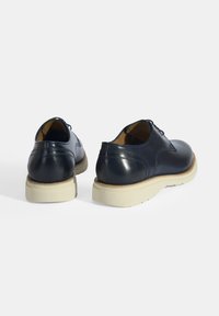 Marine leren schoenen met een gladde afwerking, ronde neus en witte rubberen zool. Bevat minimale stiksels en een klassiek ontwerp voor veelzijdigheid.