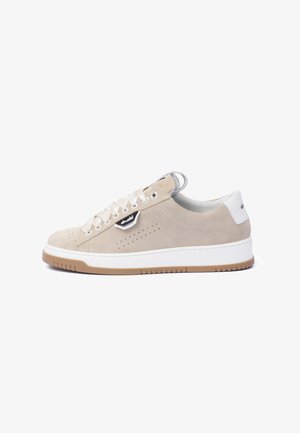 Beige suede sneaker featuring a white rubber sole, round toe, prominent lacing, side perforations, and a black and white logo accent.