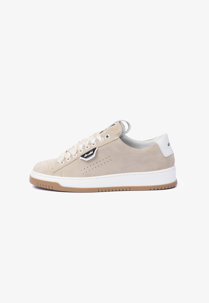 Beige suede sneaker featuring a white rubber sole, round toe, prominent lacing, side perforations, and a black and white logo accent.