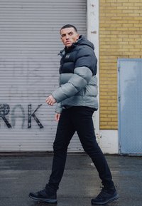 Gevoerde pufferjack met een zwarte bovenkant en grijze onderkant, voorzien van een capuchon en rits. Slimme zwarte broek en zwarte geprofileerde boots.