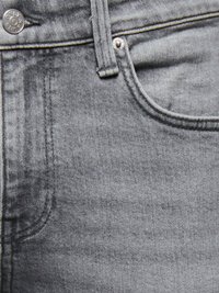 Gros plan sur un jean en denim gris montrant un bouton en métal, une passants de ceinture, un rivet et les bords supérieurs des poches avant avec des coutures détaillées.