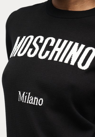 Pull en tricot noir avec un grand texte blanc "MOSCHINO" sur la poitrine et un plus petit texte blanc "Milano" en dessous.