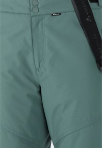 Gröna vattentäta byxor med en slät struktur, utrustade med två knappar i midjan, fickor och ett justerbart svart band med varumärke.