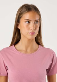 T-shirt rosa chiaro a maniche corte con scollo rotondo e texture liscia. Design semplice senza motivi né accenti aggiuntivi.