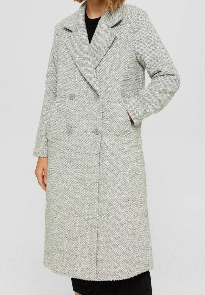 Long light gray textured double-breasted coat with notch lapels, front pockets, and four buttons, worn over a black ribbed garment.
