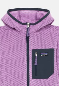 Violeta flīsa jaka ar teksturētu zīmogojumu, tumši zila kapuce un rāvējslēdzēja priekšējā kabata, ar logotipu uz krūtīm.