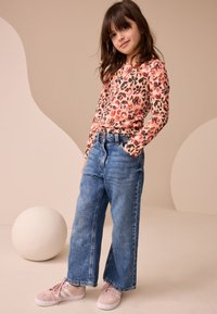 Leopard-print long-sleeve top in pink and orange tones, paired with blue wide-leg denim jeans and light pink sneakers.