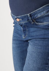 Dark blue denim jeans featuring a mid-rise waist, sturdy stitching, a metal button, and a smooth texture around the belly area.
