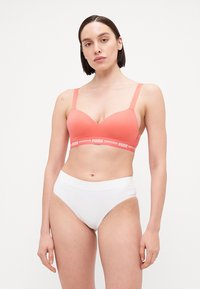Coral sports bra with adjustable straps, padded cups, and a PUMA logo band. Paired with simple white high-waisted underwear.