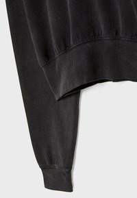 Felpa nera con vestibilità rilassata, caratterizzata da un colletto e polsini a coste, una texture morbida e una finitura leggermente sbiadita.