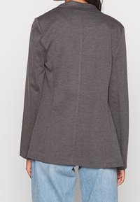 Harmaa bleiseri, jossa pitkät hihat, istuva leikkaus, hienovarainen kangaspinta, takana yksittäinen halkio, yhdistetty vaaleansinisiin löysästi istuviin farkkuihin.