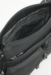 Schwarze Stofftasche mit mehreren mit Reißverschluss versehenen Fächern und einem glatten Innenfutter mit einem Logomuster. Robustes Material und deutlich sichtbare Nähte.