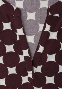 Détail du col en tissu avec de grands cercles bordeaux foncé et de petits losanges blancs formant un motif géométrique.