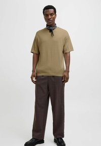Kortærmet olivengrøn t-shirt sammen med brune ternede bukser. Accessoriseret med et sort og hvidt bandana. Glat bomuldsstruktur.