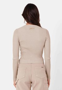 Beige ribbad långärmad topp med rund halsringning, med subtila vertikala ränder och en liten logotypdetalj bak.