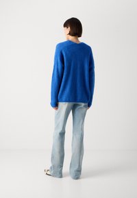 Blue knitted sweater with a loose fit and V-neck, paired with light blue flared jeans, showing a textured finish and casual design.