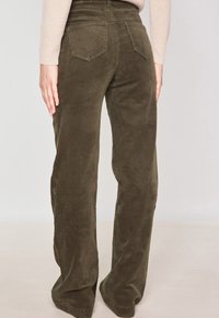 Pantalons en velours côtelé verts avec un design évasé et un tissu texturé, dotés de poches arrière. La taille est haute et le bas des jambes est ajusté.