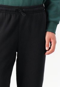 Svarte joggebukser med elastisk midje og justerbar snor. Myk tekstur, smale ben og synlige sidelommer.