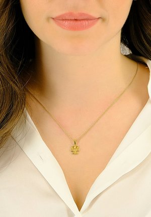 Femme portant un collier en or avec un pendentif en forme de balance de la justice et une blouse blanche, montrant les lèvres et la zone du cou.