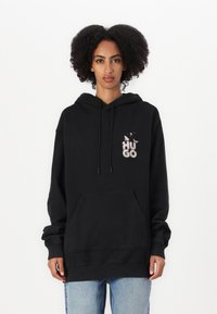 Svart hettegenser med frontlomme, med en strukturert "HUGO"-logo på brystet. Laget av mykt stoff, med ribbede ermer og hem.