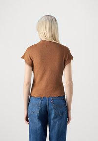 Brun strikket top med korte ærmer og bølget kant, parret med blå denim jeans med et Levis-mærke på baglommen.