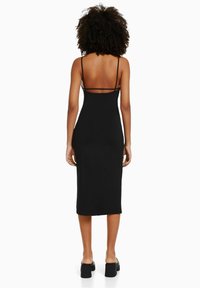 Robe midi noire à fines bretelles, silhouette ajustée et dos décolleté. Texture lisse, polyvalente pour diverses occasions.