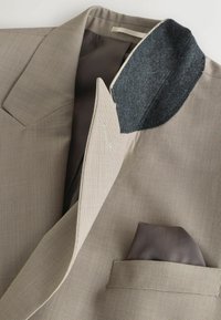 Blazer marron clair texturé avec sous-col en feutre gris foncé et pochette gris foncé dans la poche poitrine.
